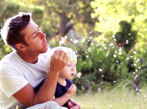 father and child blowing dandelion seeds